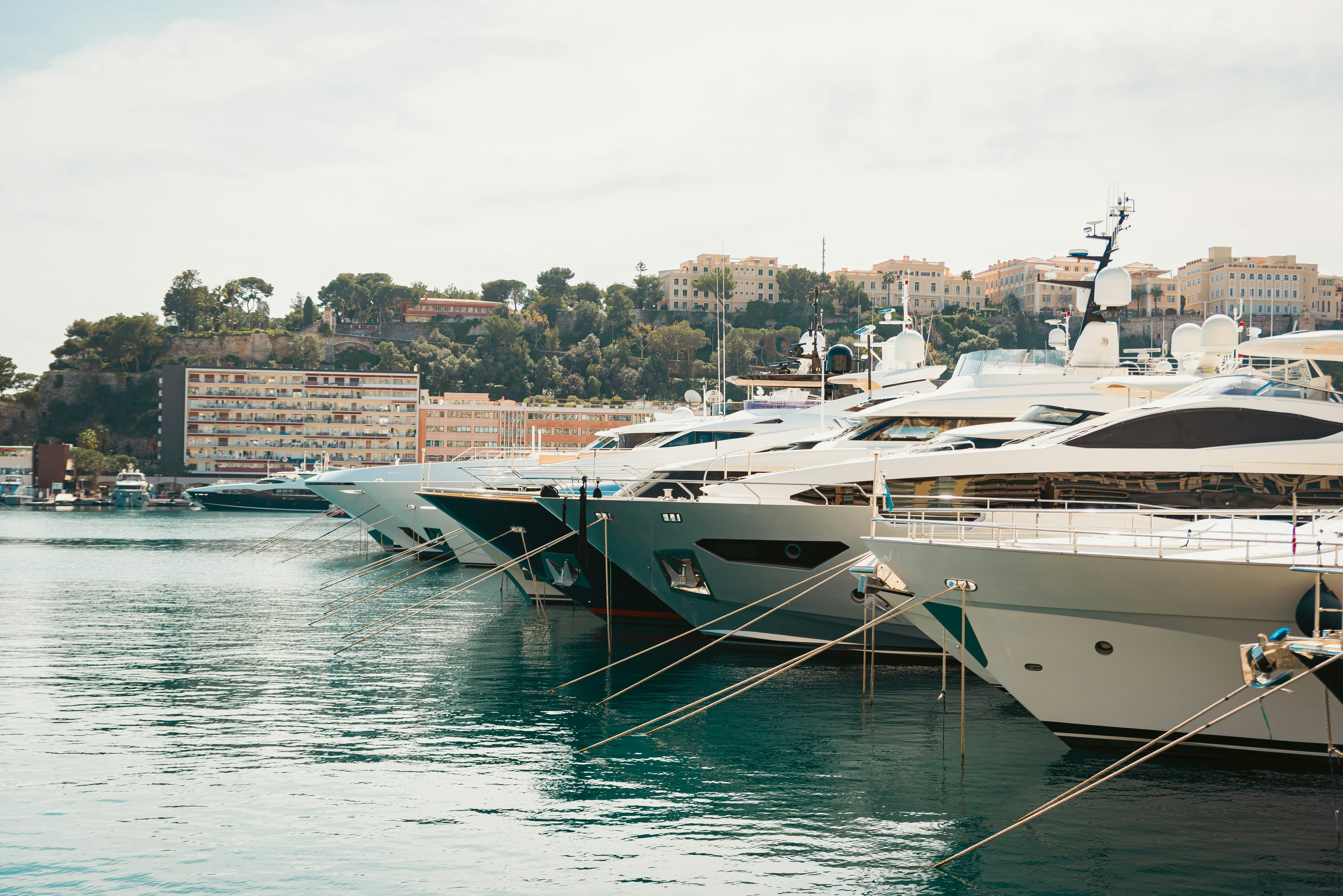 A row of moored superyachts in Port Hercule, Monaco, with the Monte Carlo hillside behind